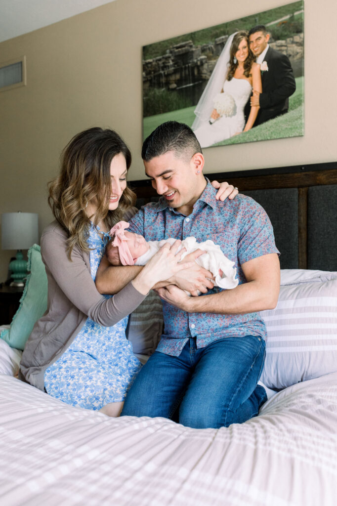 Parents kneeling on their bed holding and looking at their newborn baby.