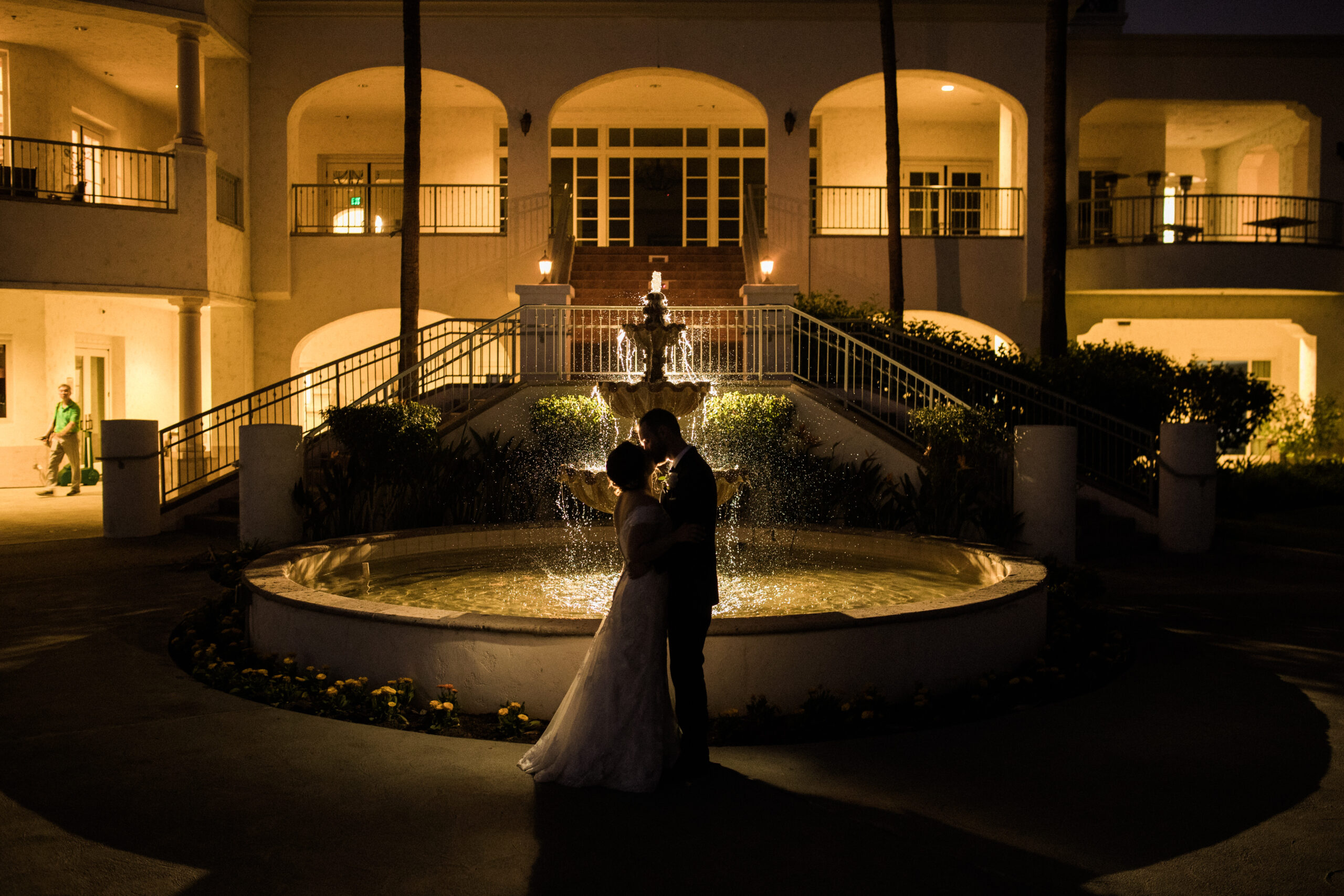 Bride and Groom share an intimate kiss in front of Los Coyotes Country Club wedding venue in Buena Park at night with the dim lights in the background.